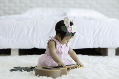 Baby girl wearing headband playing with guitar while sitting on rug at home