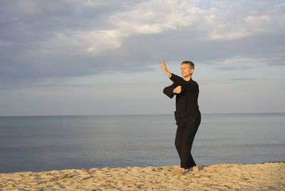 Mature man practicing tai chi at beach against sky