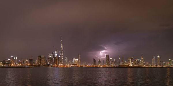 Illuminated city by river against sky at night