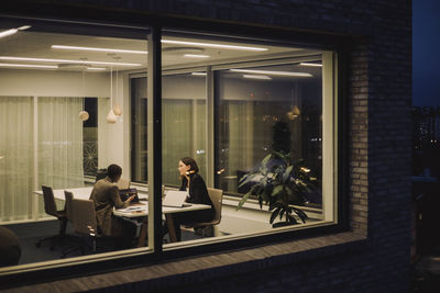 Businesswoman discussing with female colleague over laptop working late in office