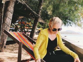 Woman wearing sunglasses sitting on seat against trees