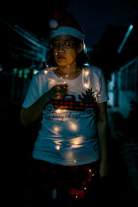 Portrait of young woman standing against black background