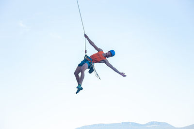 Low angle view of man hanging from rope against clear sky