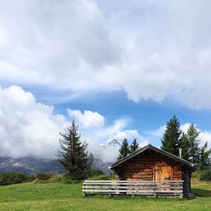 House on grassy field against cloudy sky