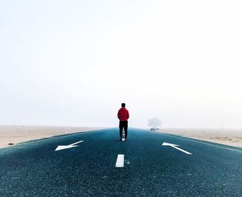 Rear view of man standing on road against sky