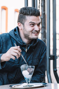 Smiling young man eating ice cream while sitting at restaurant