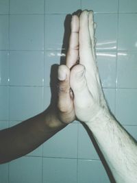 Close-up of cropped hands clasped against tiled wall