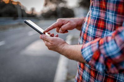 Close-up view of businessman  walking in the street and typing messages on his mobile phone. 