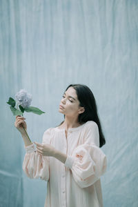 Young woman holding white flower standing against plants