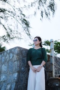 Woman looking away while standing by stone wall against sky