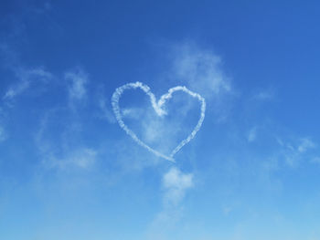 Low angle view of heart shape vapor trail in blue sky