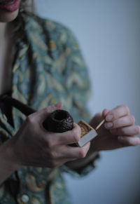 Midsection of mid adult woman holding matchstick and pipe while standing against wall