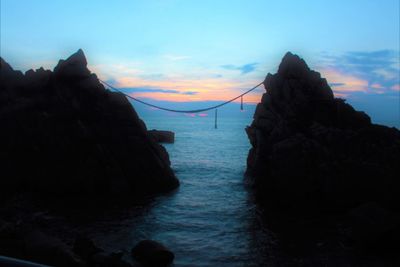 Silhouette rocks by sea against sky during sunset