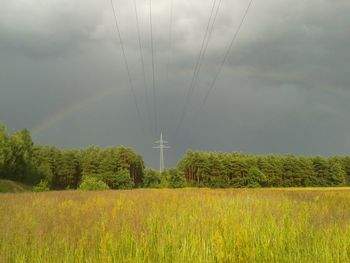 Electricity pylon on field against cloudy sky