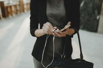 Midsection of woman holding mobile phone and purse while standing in cafe