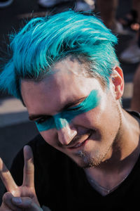 Close-up portrait of young man with dyed hair showing peace sign