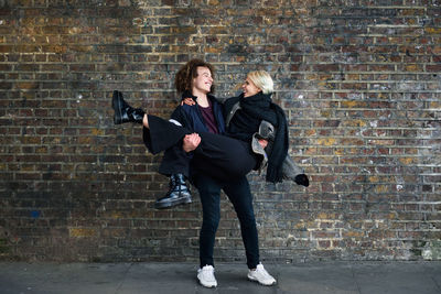 Happy boyfriend carrying girlfriend while standing against brick wall