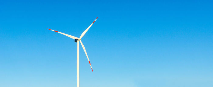 Low angle view of windmill on landscape against blue sky