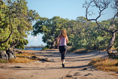 Woman running on street amidst trees against sky