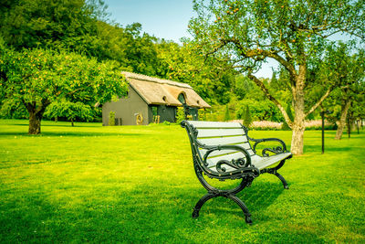 Park bench on field by trees against sky