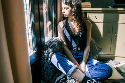 Young woman looking down while sitting on window