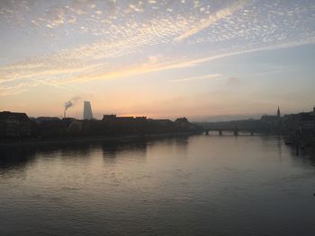 Scenic view of river by buildings against sky during sunset