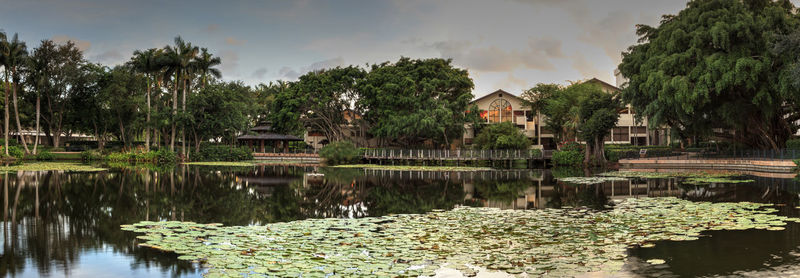 Scenic view of lake by trees and houses against sky