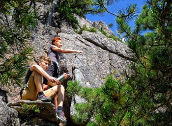 Low angle view of friends sitting on rock against trees