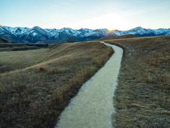 Empty road leading towards snowcapped mountains against sky