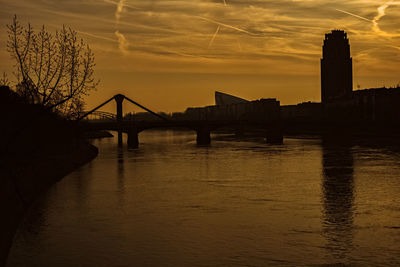 Silhouette bridge over river against sky during sunset