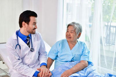 Smiling doctor sitting by senior woman in hospital