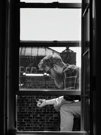 Side view of lumbersexual man smoking cigarette by window