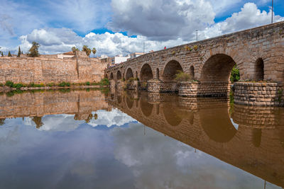 Arch bridge over river against cloudy sky