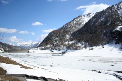 Scenic view of frozen lake by mountains against sky