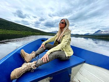 Woman sitting by lake against sky