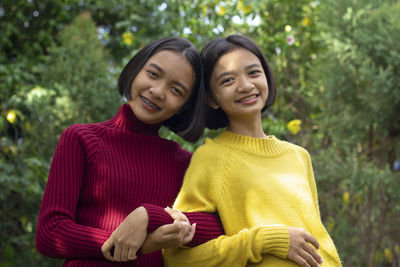 Portrait of smiling teenage girl standing with friend against trees