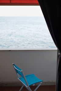 Chairs by sea against sky seen through window