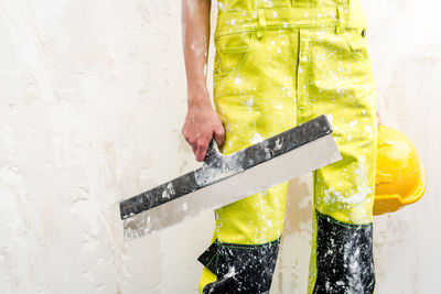 Midsection of female construction worker holding squeegee while standing against wall