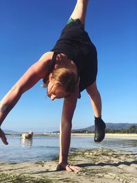 Woman practicing handstand at beach against clear sky