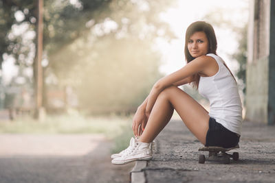 Portrait of smiling young woman sitting on skateboard outdoors