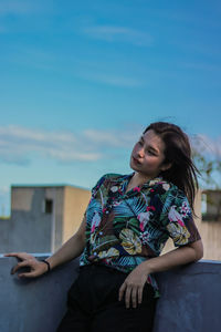 Beautiful young woman sitting against blue sky
