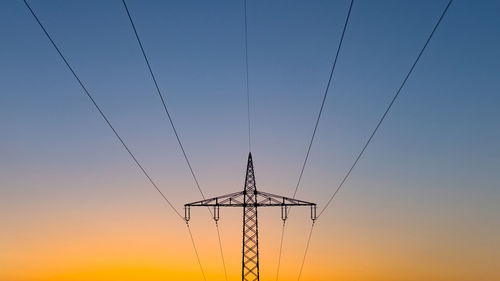 Low angle view of electricity pylon against sky during sunset