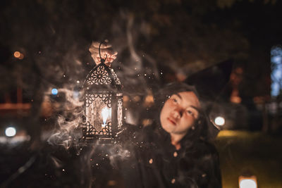 Young woman holding illuminated lantern at night