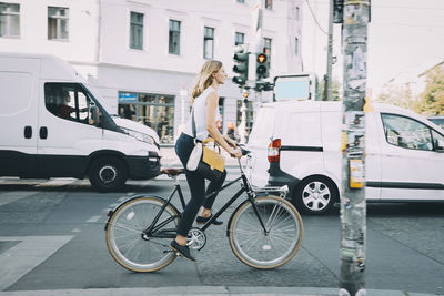 Full length of young businesswoman riding bicycle on road in city