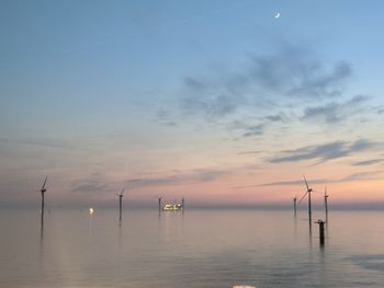 Scenic view of sea against sky during sunset with wind turbine