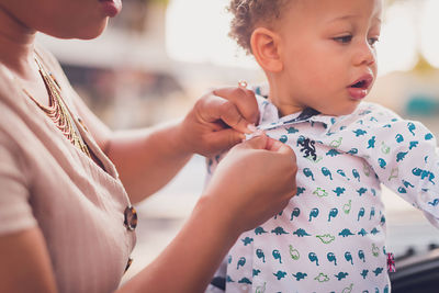 Mom buttoning baby boy's shirt, close up to hands and boy's face.