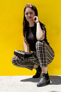 A young latin woman sitting and smiling, wearing casual clothes, yellow background