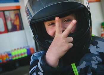 Close-up portrait of boy wearing crash helmet gesturing peace sign