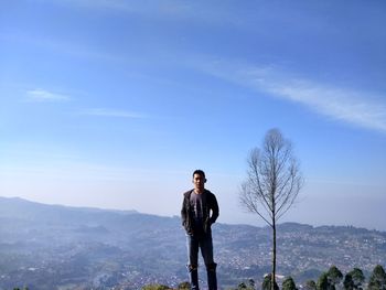 Young man standing on mountain against blue sky
