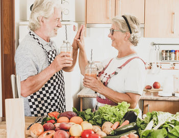 Smiling senior couple touching hands while standing at kitchen